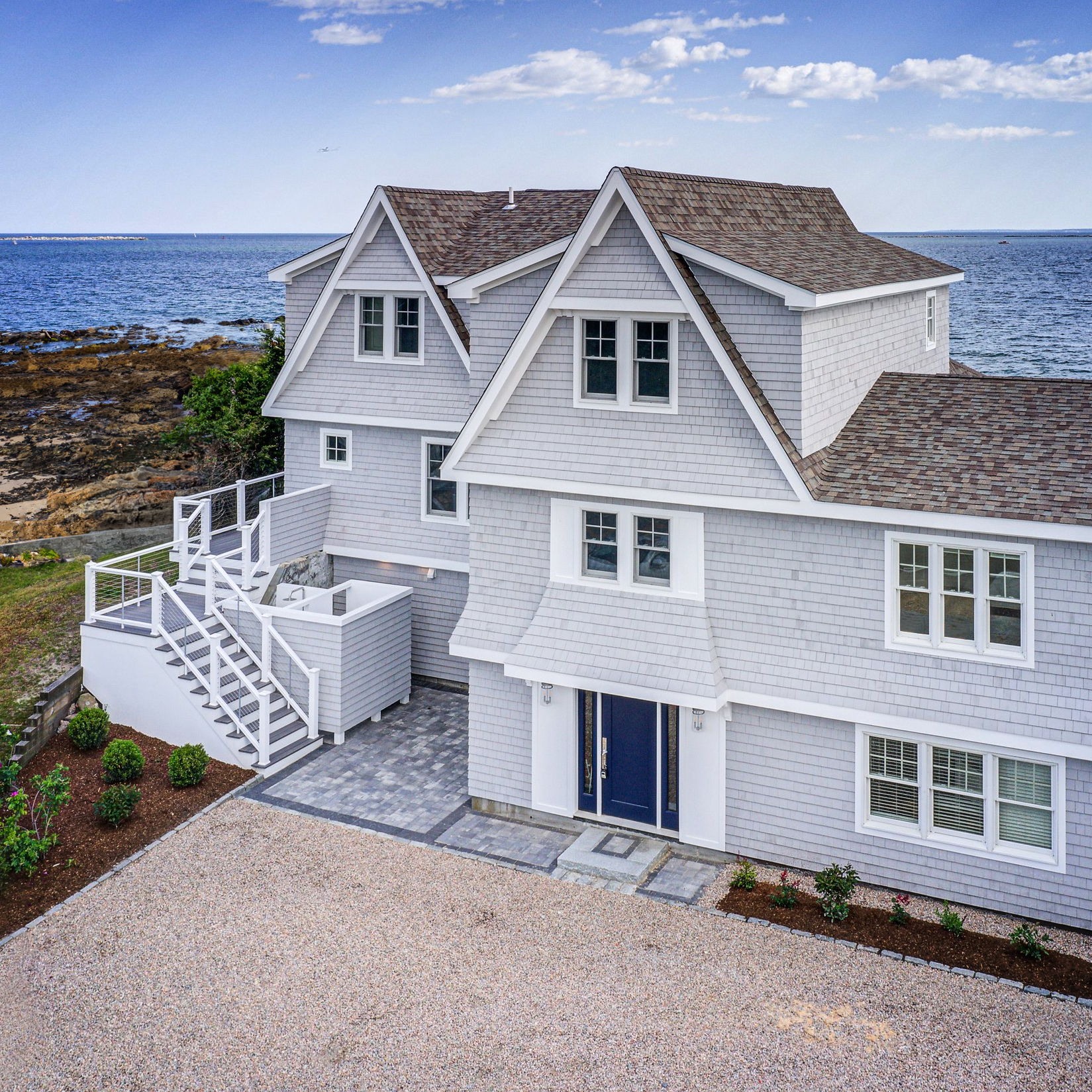 Exterior view of a three-story coastal home featuring a new third-level addition and contemporary grey shingle siding.