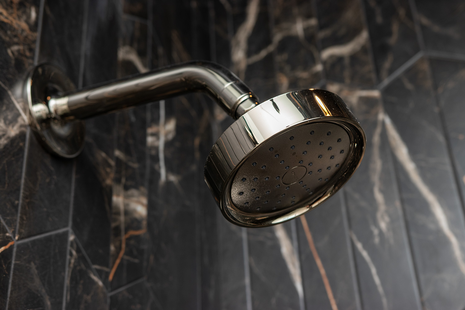 Detail of modern polished chrome fixtures against dark stone, showcasing the precision execution of Hill & Harbor's design-build team.
