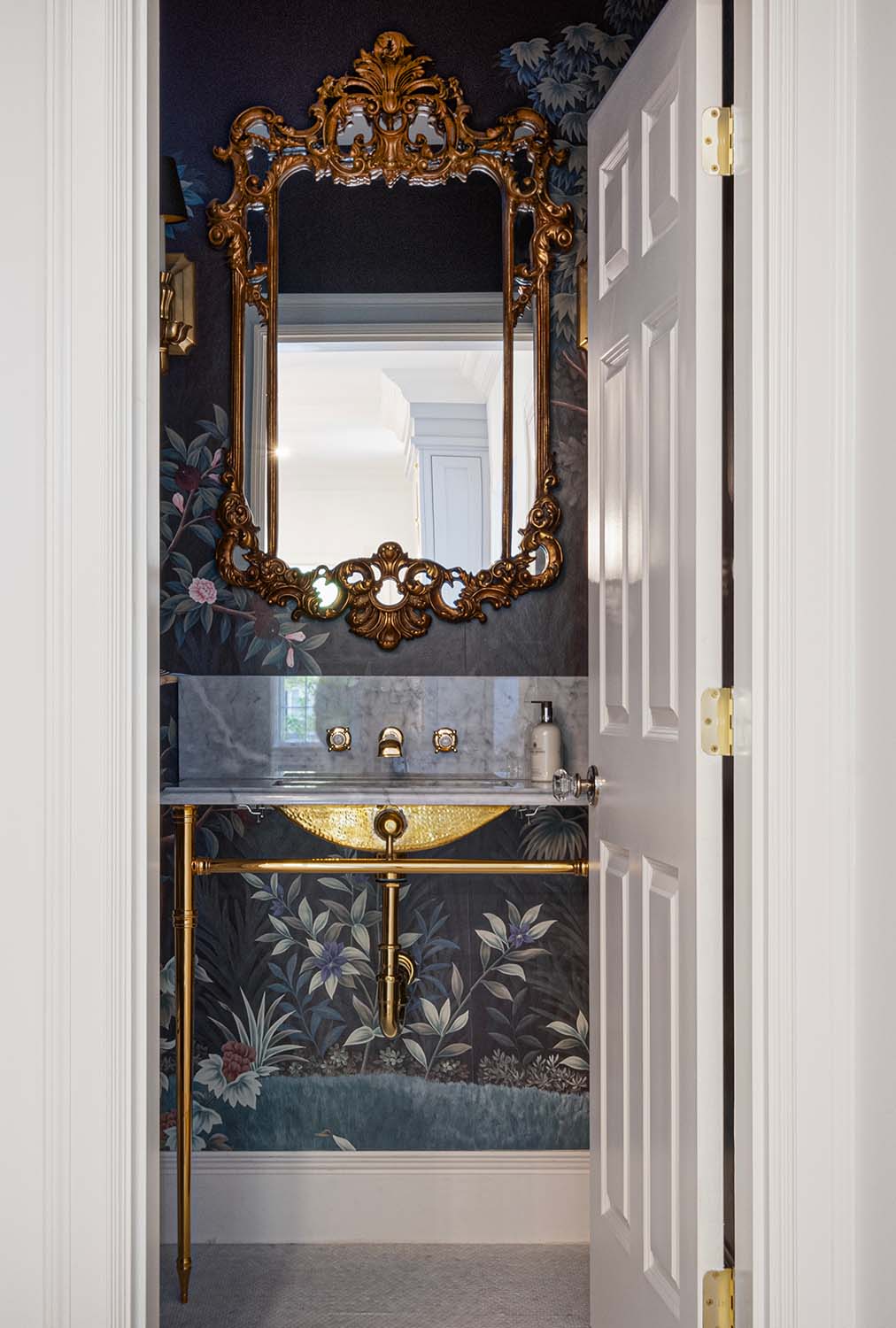 Ornate powder room featuring a gold mirror, brass washstand, and intricate wallpaper.