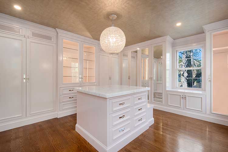 Expansive master closet renovation featuring a center island, glass-front cabinetry, and boutique-style lighting.