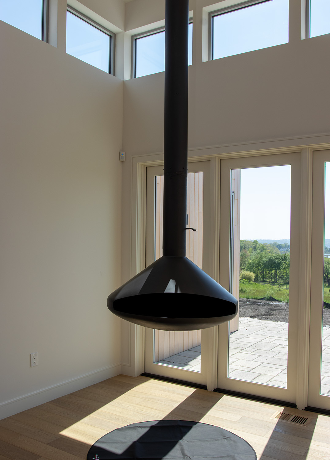 A striking contemporary hanging fireplace in a Tiverton, RI home, framed by floor-to-ceiling windows overlooking the Sakonnet River.