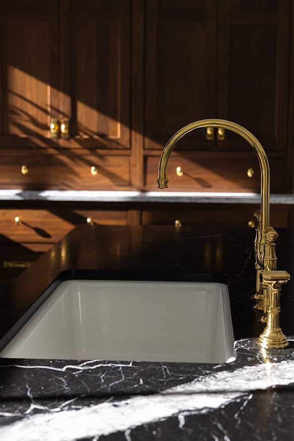 Luxury kitchen sink detail featuring a marble apron front sink and a high-end brass bridge faucet.