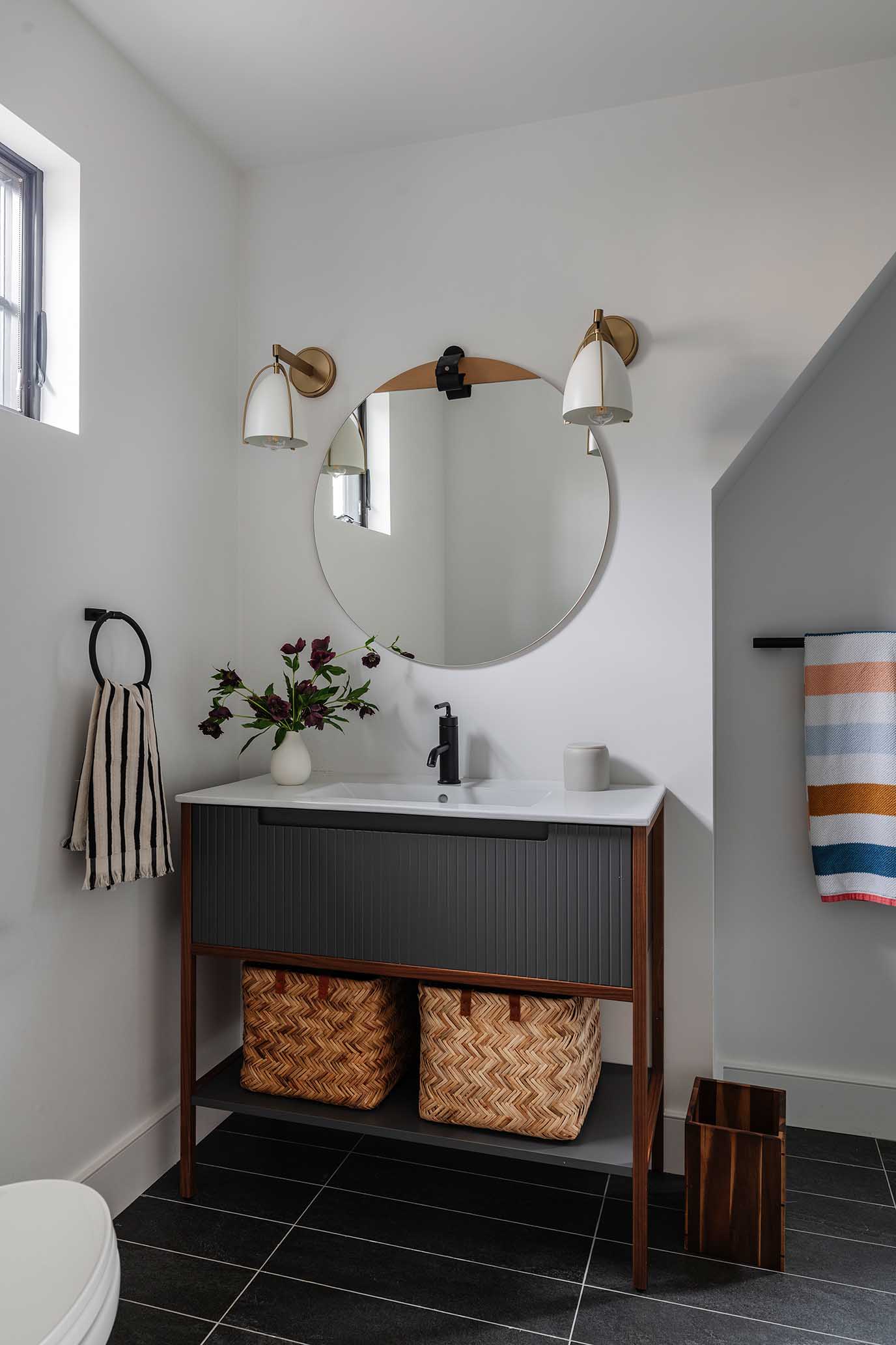 Charming powder room design with a dark vanity and round mirror, blending modern and traditional styles.