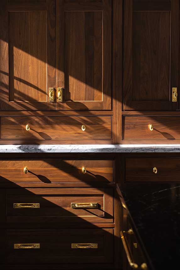 Sunlit detail of custom wood cabinetry and unlacquered brass hardware.