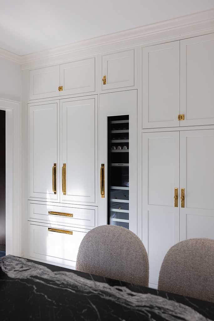 Floor-to-ceiling white pantry cabinetry with integrated appliances and brass pulls.